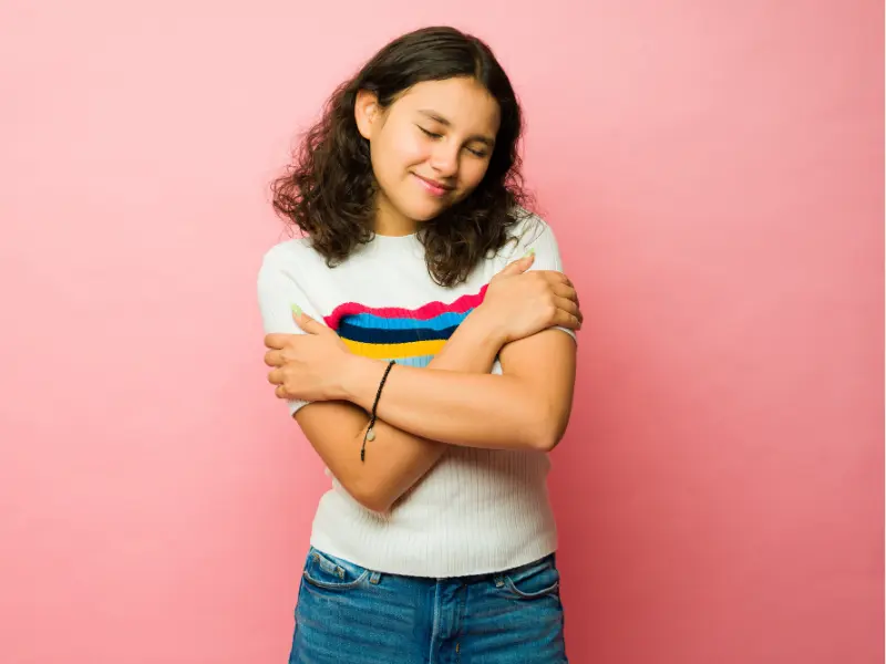 A woman standing peacefully, hugging herself with a gentle smile, symbolizing self-love, a positive self-image, confidence, and the beginning of a successful weight loss journey.